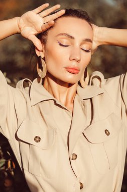 Yüzünde güzel makyajlı, etkileyici yüz hatları ve vücudu olan güzel esmer bir kız. Sonbaharda güzel ağaçların arasında şık bir takım elbise giyiyor.