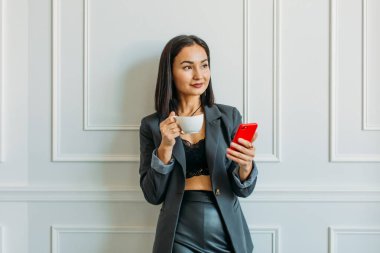 Asyalı görünümlü genç ve güzel bir kız. Evde web konferansı düzenliyor. Dizüstü bilgisayarı ve elinde telefonu var.