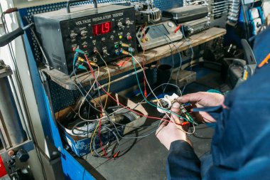 Araba tamirhanesinde çalışan bir işçi jeneratörü test eder ve tamir eder.