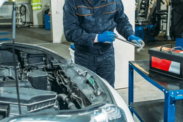 the process of replacing the car battery in the garage, a worker removes the old battery, replaces and tests a new battery.