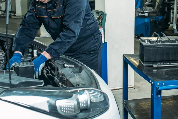 the process of replacing the car battery in the garage, a worker removes the old battery, replaces and tests a new battery.