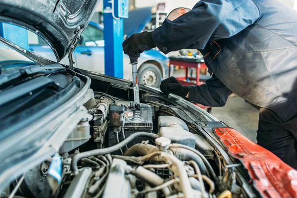 a worker in a car repair shop stands in front of the car, the hood of the car is open, the worker inspects and tests the car