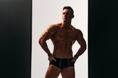 Güçlü bünyesi olan genç bir adam güzel gövdeli bir vücut geliştirici figürüne sahip. Stüdyoda siyah beyaz bir arkaplanda çekim yapmak. titreşimli ışık.