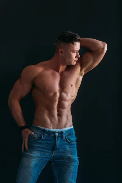 A young Man of strong constitution with a relief figure of a bodybuilder with a beautiful torso. Shooting in the studio on a black background.