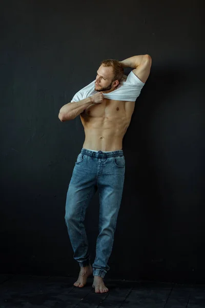 A young Man of strong constitution with a relief figure of a bodybuilder with a beautiful torso. Shooting in the studio on a black background.