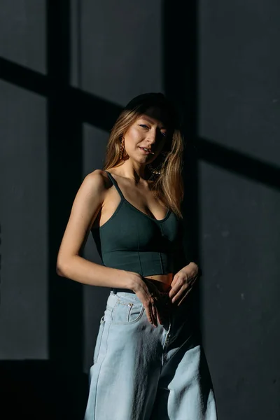 若い美少女は体の形がよく上とジーンズに黒い背景のスタジオで窓からの日光 — ストック写真