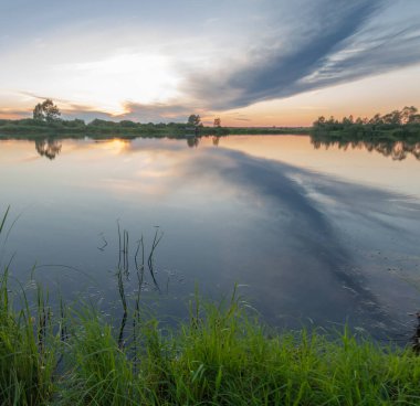 Rusya 'nın Bashkortostan cumhuriyetinin Agidel kasabasındaki küçük nehrin yakınındaki bir ormanda günbatımının tadını çıkarıyorum.