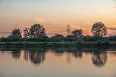 Rusya 'nın Bashkortostan cumhuriyetinin Agidel kasabasındaki küçük nehrin yakınındaki bir ormanda günbatımının tadını çıkarıyorum.