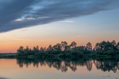 Rusya 'nın Bashkortostan cumhuriyetinin Agidel kasabasındaki küçük nehrin yakınındaki bir ormanda günbatımının tadını çıkarıyorum.
