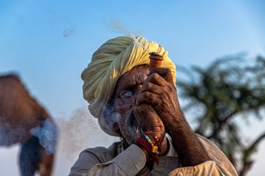 Kasım 2019 Pulkar Rajasthan: Pulkar deve festivalinde chiilam tüttüren yaşlı bir kabilenin portresi