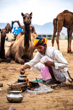 Geleneksel giysili bir adam grubu için yemek yapmakla meşgul..