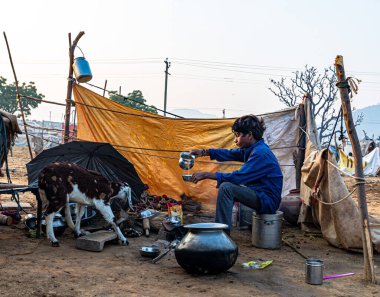 Bir çocuk çaydanlığa sabah çayı dolduruyor, açık mutfağında oturuyor ve keçisi de yanında..