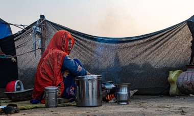 Kimliği belirsiz göçebe kadın açık mutfakta yemek yapıyor, tencere ve tavalar pişirmek için doğal ateşte yanıyor..