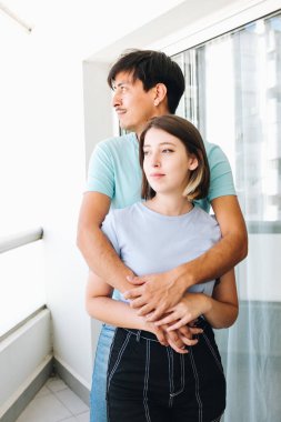 Genç çift balkonda sarılıyor.