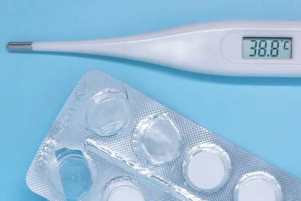 Dijital termometre yüksek sıcaklığı ve mavi arka planda kullanılan tabletleri gösteriyor. covid önleme kavramı