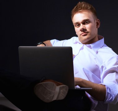 Gri arka plan üzerinde dizüstü bilgisayar konumu olan kendine güvenen genç adam portresi