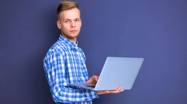 Portrét sebevědomý mladý muž s notebook stojící nad šedým pozadím — Stock fotografie