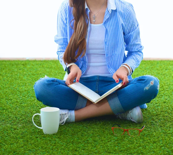 Mladá žena sedí s knihou na trávě — Stock fotografie