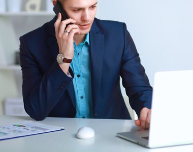 Genç işadamı ofiste çalışıyor, masada oturuyor.