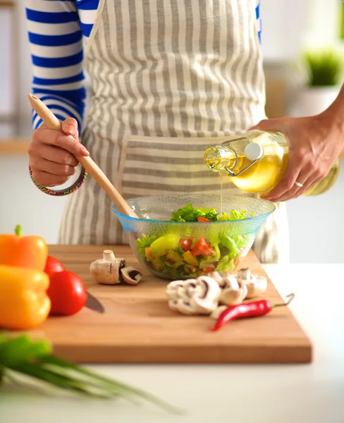 Jovem mulher misturando salada fresca de pé perto da mesa — Fotografia de Stock