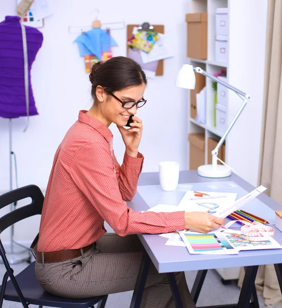 Ofis masasında çalışan genç, çekici bayan moda tasarımcısı, cep telefonuyla konuşurken çizim yapıyor. — Stok fotoğraf