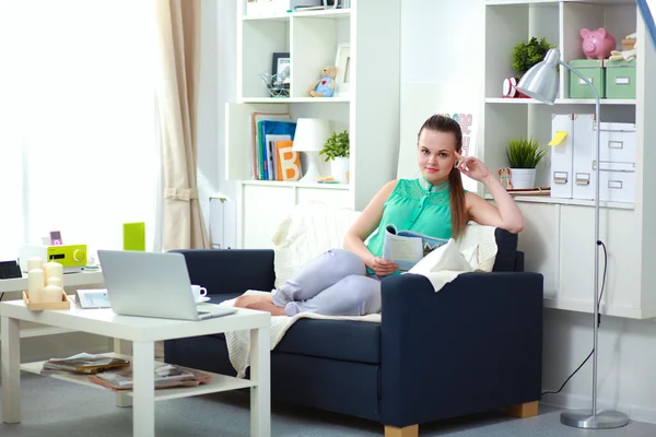 Hermosa joven sentada en el sofá y leyendo —  Fotos de Stock