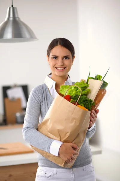 ผู้หญิงสาวถือถุงช้อปปิ้งกับผัก ยืนอยู่ในครัว — ภาพถ่ายสต็อก