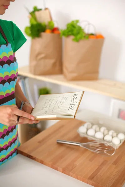 Jovem mulher lendo livro de receitas na cozinha, à procura de receita — Fotografia de Stock