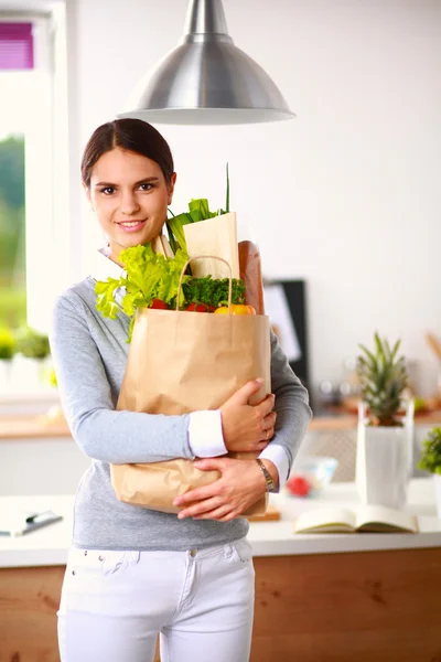 Jovem mulher segurando supermercado saco de compras com legumes .Standing na cozinha — Fotografia de Stock