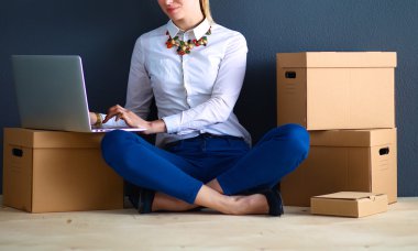 Kadın yerde dizüstü bilgisayarlı bir kutunun yanında oturuyor.