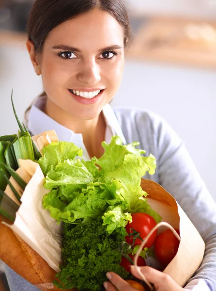 Giovane donna che tiene borsa della spesa con verdure. In piedi in cucina — Foto Stock