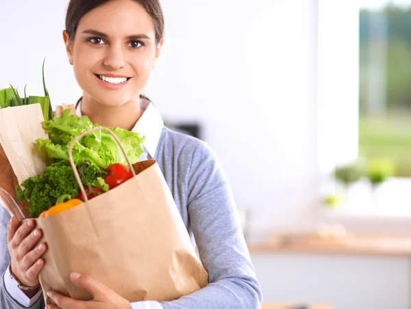 Giovane donna che tiene borsa della spesa con verdure. In piedi in cucina — Foto Stock