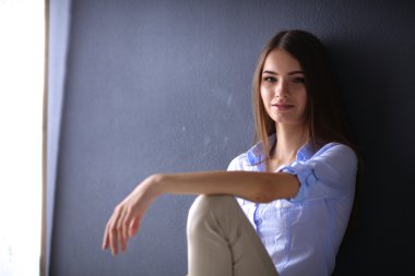 Genç bir kadın yerde, kara duvarın yanında oturuyor.