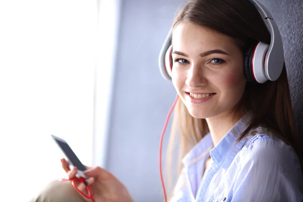 Ragazza sorridente con le cuffie seduto sul pavimento vicino al muro — Foto Stock