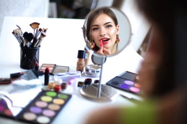 Jeune belle femme se maquillant près du miroir, assise au bureau — Photo