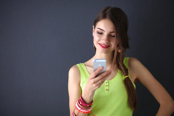 Mujer joven de pie cerca de la pared oscura con teléfono — Foto de Stock