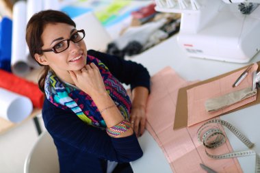 Güzel moda tasarımcısı stüdyoda masada oturuyor.