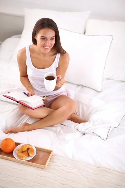Νεαρή όμορφη γυναίκα κάθεται στο κρεβάτι και τη γραφή σε ένα τετράδιο — Φωτογραφία Αρχείου
