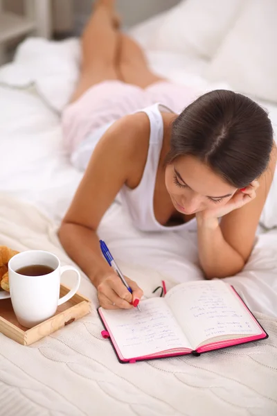 Όμορφη κοπέλα ξαπλωμένη στο κρεβάτι, γράφοντας ένα ημερολόγιο — Φωτογραφία Αρχείου