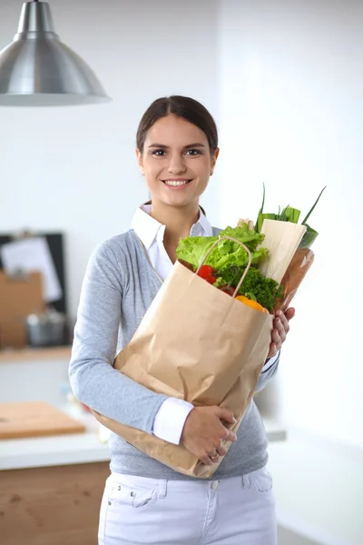 Giovane donna che tiene borsa della spesa con verdure. In piedi in cucina — Foto Stock