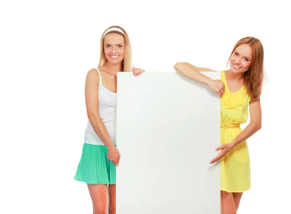Retrato de dos mujeres jóvenes casuales de pie cerca de la tarjeta en blanco sobre fondo blanco — Foto de Stock