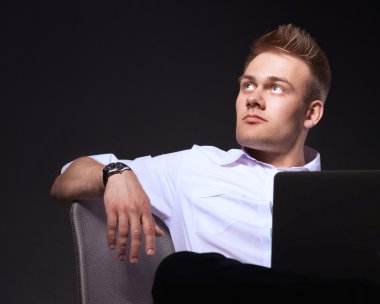 Gri arka plan üzerinde dizüstü bilgisayar konumu olan kendine güvenen genç adam portresi