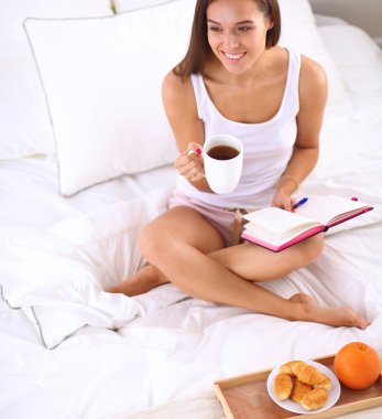 Yatakta oturmuş ve bir defterini yazma genç güzel kadın