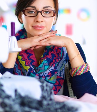 Güzel moda tasarımcısı stüdyoda masada oturuyor.