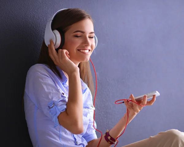 Uśmiechnięte dziewczyny ze słuchawkami, siedząc na podłodze w pobliżu ściany — Zdjęcie stockowe
