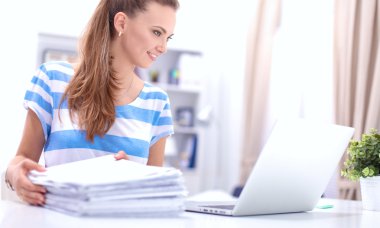 Elinde evrakları olan kadın masanın üstünde oturuyor.