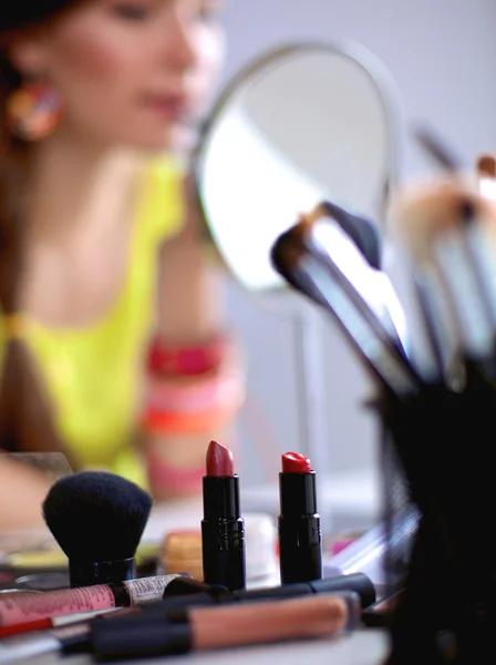 Unga vackra kvinnan att göra make-up nära spegeln, sitter vid skrivbordet — Stockfoto