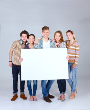 Beyaz arka planda izole edilmiş boş bir tahta tutan bir grup genç arkadaş.