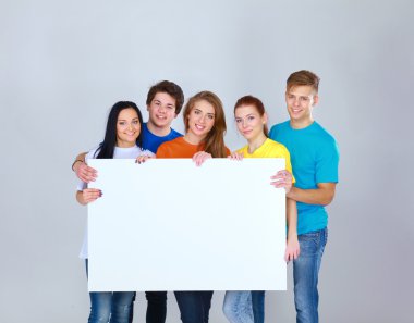Beyaz arka planda izole edilmiş boş bir tahta tutan bir grup genç arkadaş.