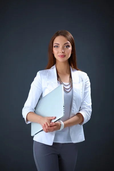 Młoda kobieta trzyma laptopa, stojąc na szarym tle — Zdjęcie stockowe